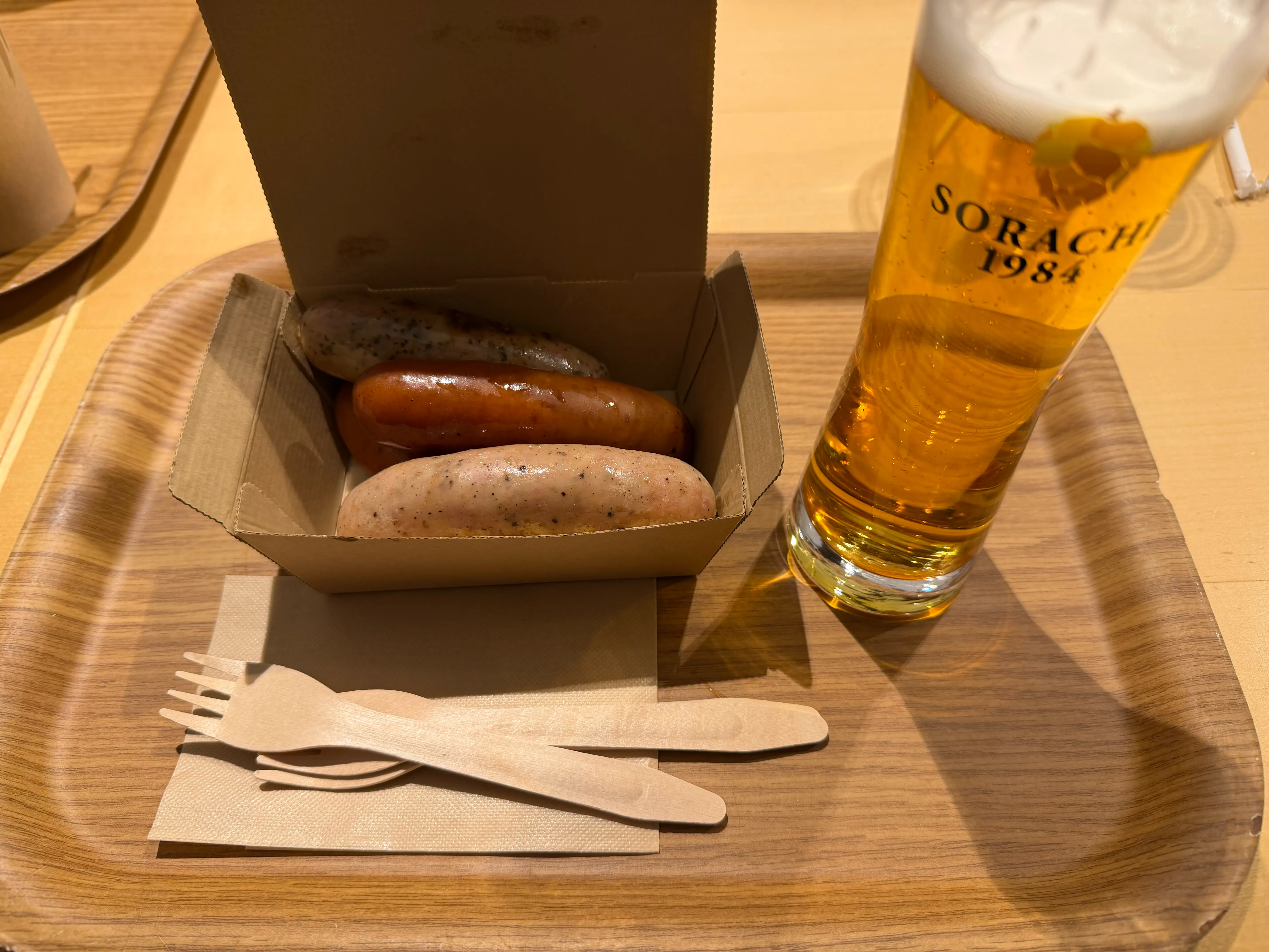 つきののソーセージ2本とSOARACHI 1984の生ビール。木製トレイに並ぶシンプルな一皿