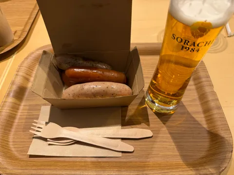 つきののソーセージ2本とSOARACHI 1984の生ビール。木製トレイに並ぶシンプルな一皿