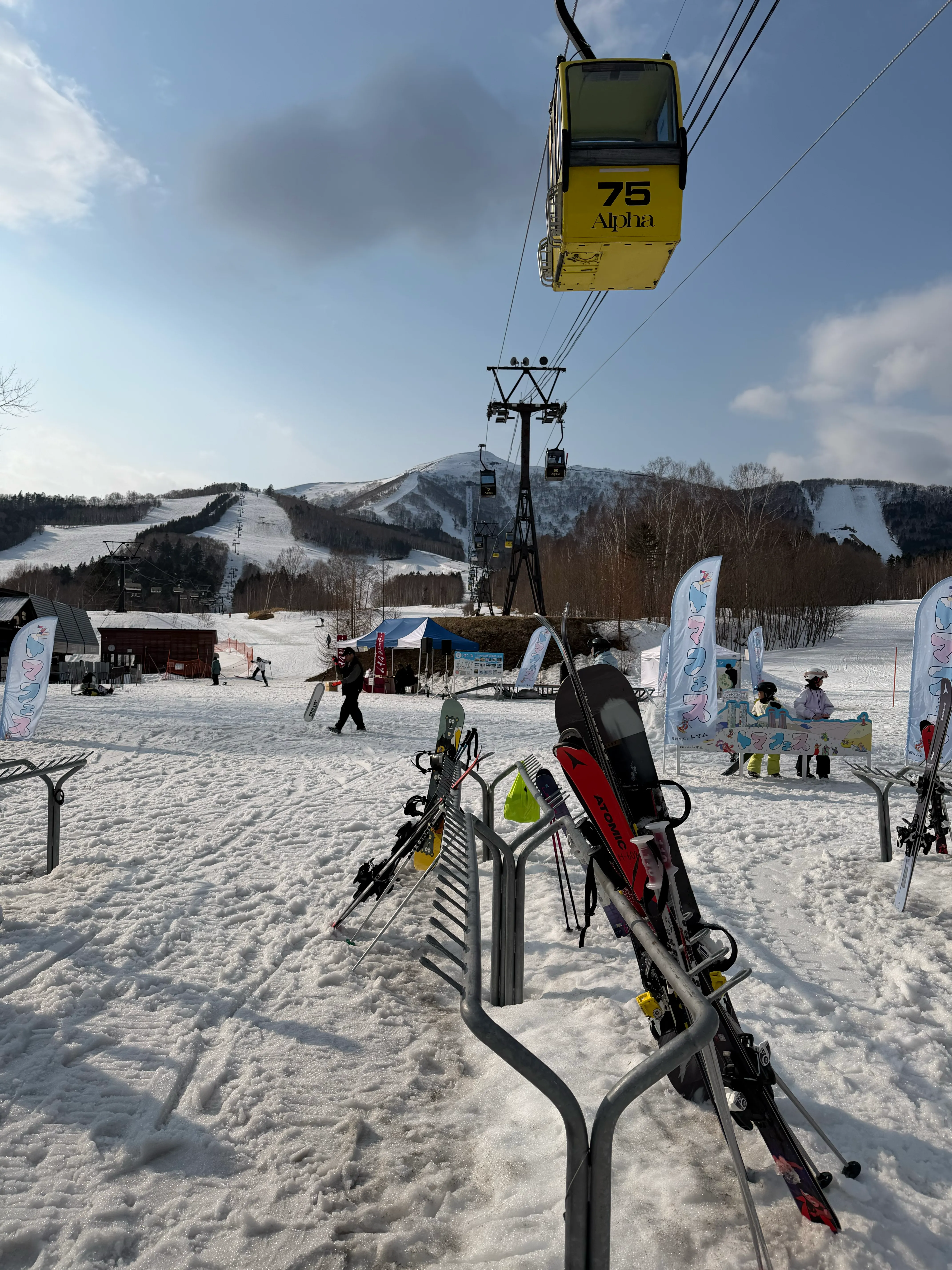 黄色い75番ゴンドラと山頂のスキー板ラック。青空が広がる