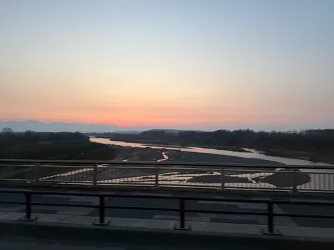 バス車窓から見える夕暮れの十勝平野。橋の上を走り抜けながら川と空のグラデーションを望む