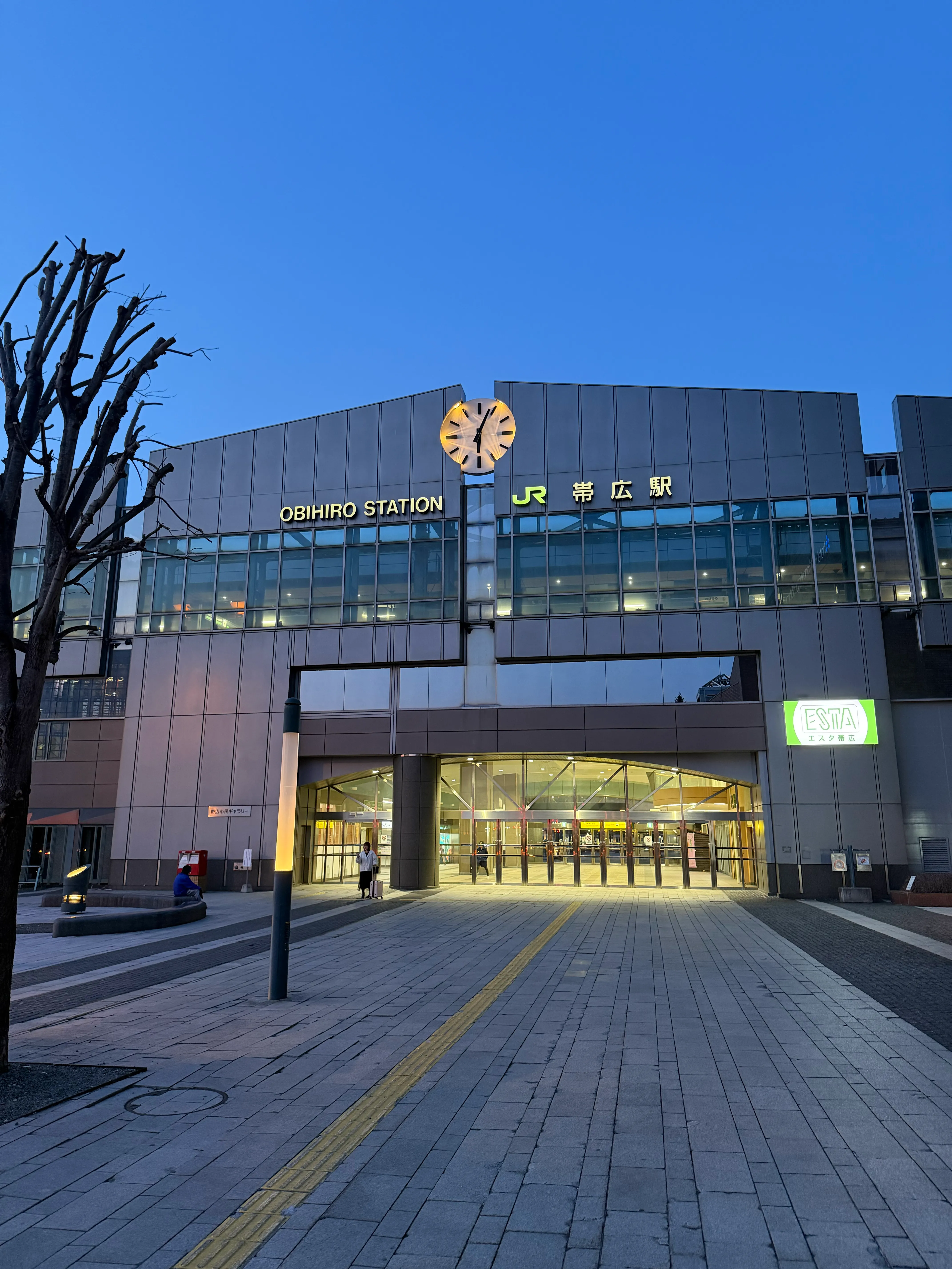 夕方の帯広駅外観。OBIHIRO STATIONの文字と時計が青い空に映える