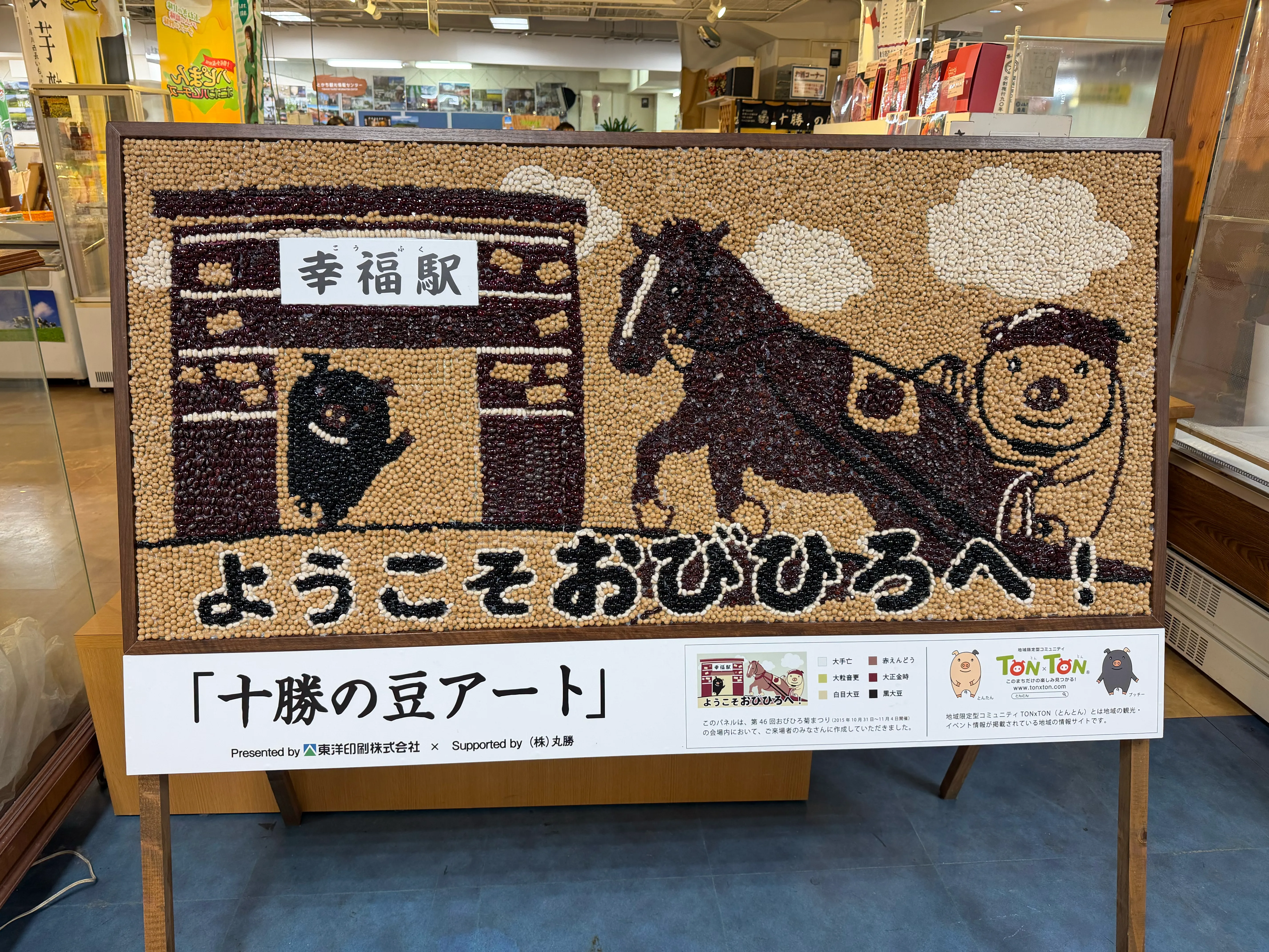 十勝の豆アート。複数種の豆を組み合わせて描かれた「ようこそおびひろへ！」のアート作品。幸福駅と馬とぶたが描かれている