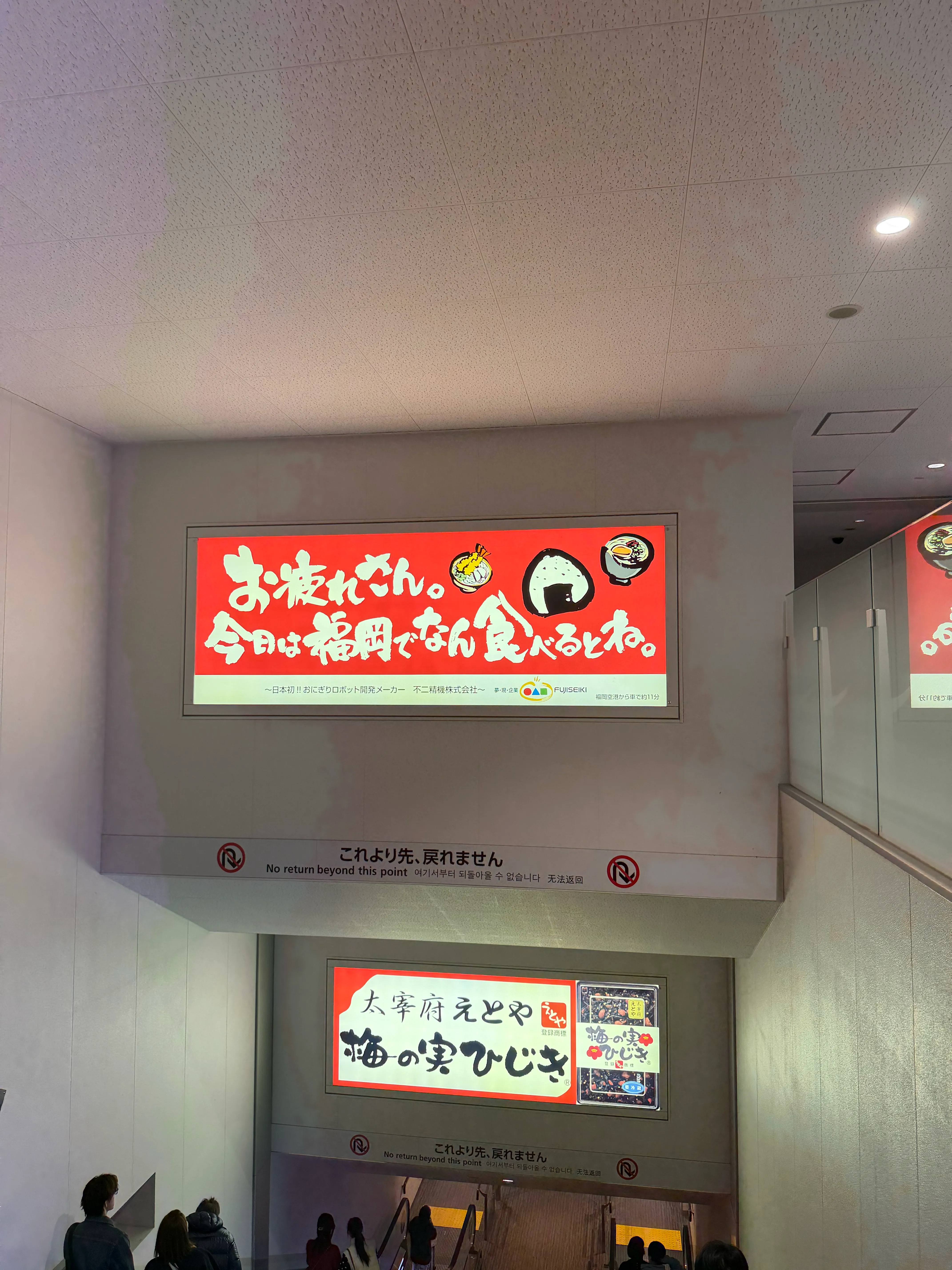 福岡空港の到着エリア。「お疲れさん。今日は福岡でなん食べるとね。」と書かれた博多弁のウェルカムメッセージが表示されたディスプレイが迎える