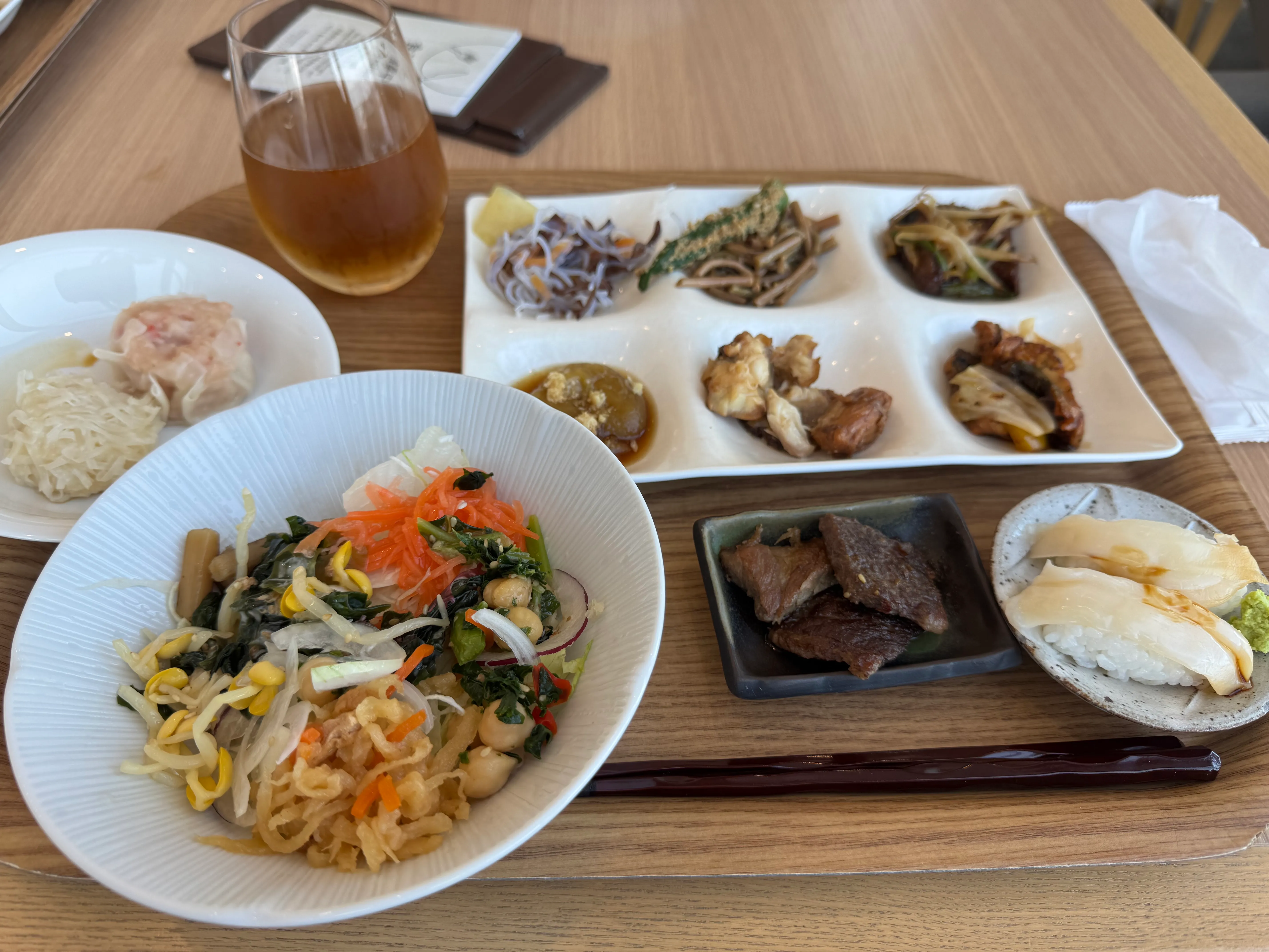 野菜炒めや小皿料理が並ぶビュッフェの取り皿と、琥珀色のビール