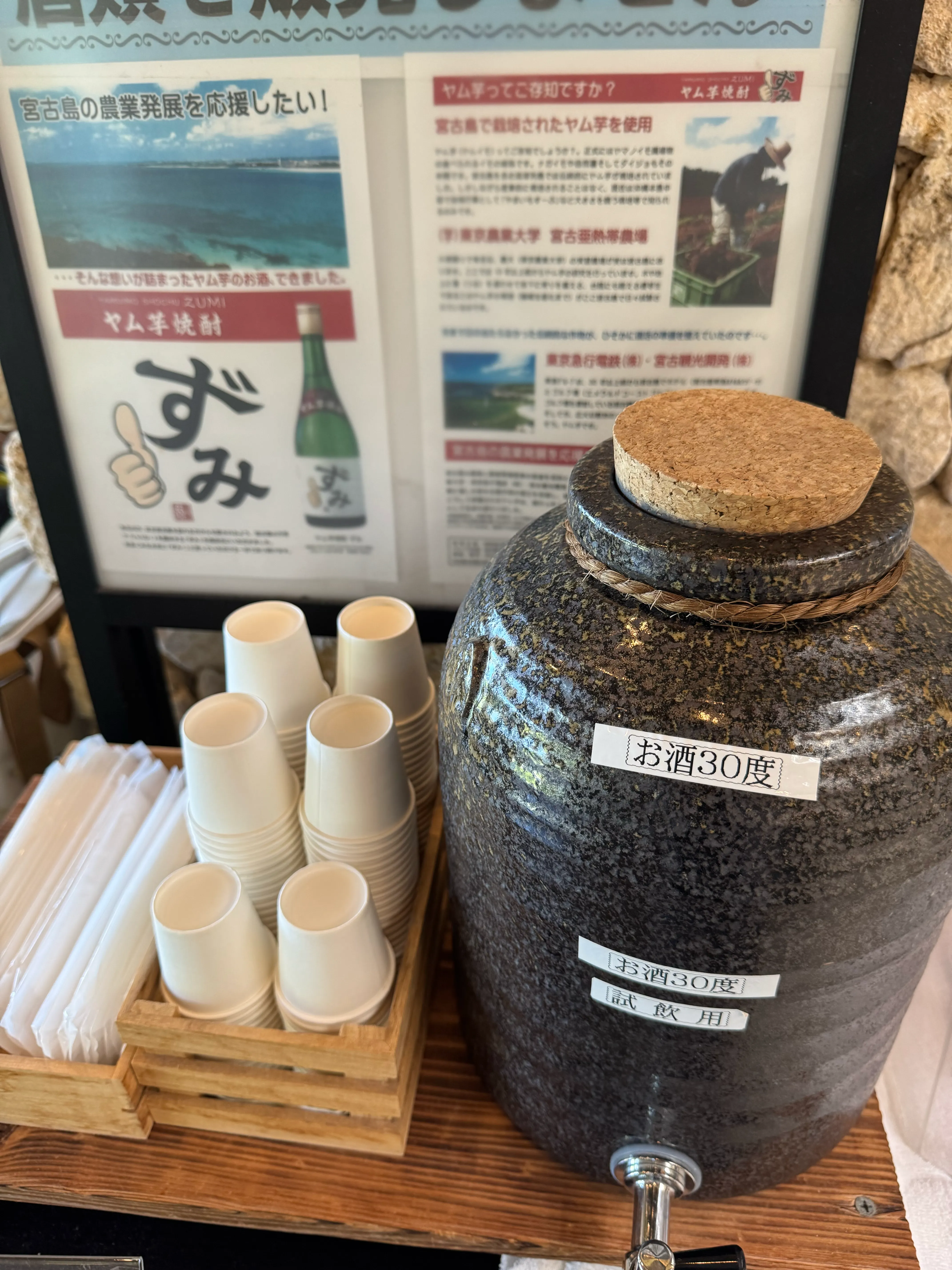泡盛30度が入った陶器の壺と紙コップ。試飲コーナーの様子