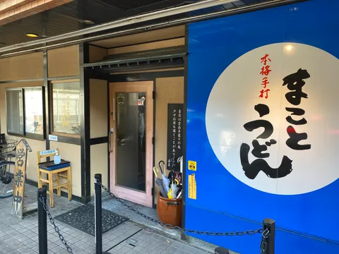 まことうどんの外観。鮮やかな青い壁に白丸で「まことうどん」と書かれた大きな看板が目を引く