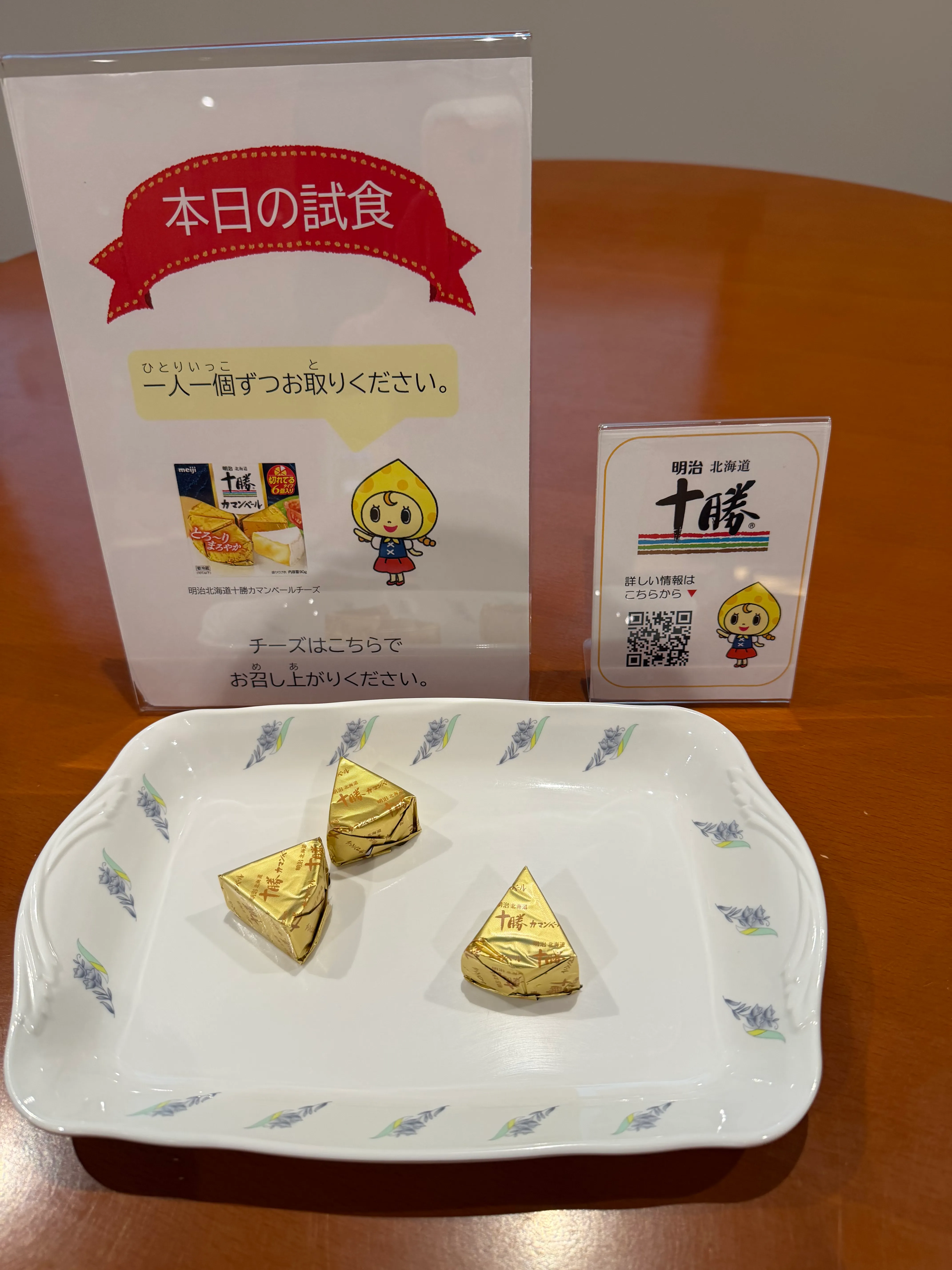 見学後にいただいた試食チーズ。アルミ包装の小さなチーズ2個と「本日の試食」プレート