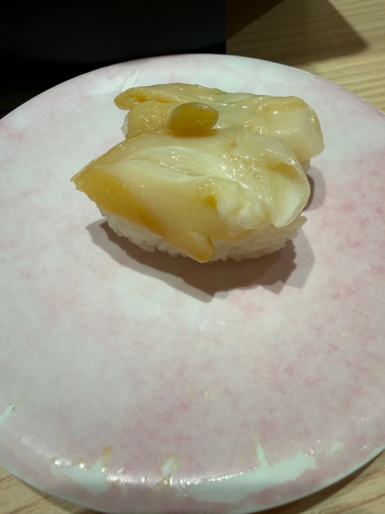 肉厚なつぶ貝の握り。ピンクの皿に乗り、大ぶりな貝がシャリからはみ出している