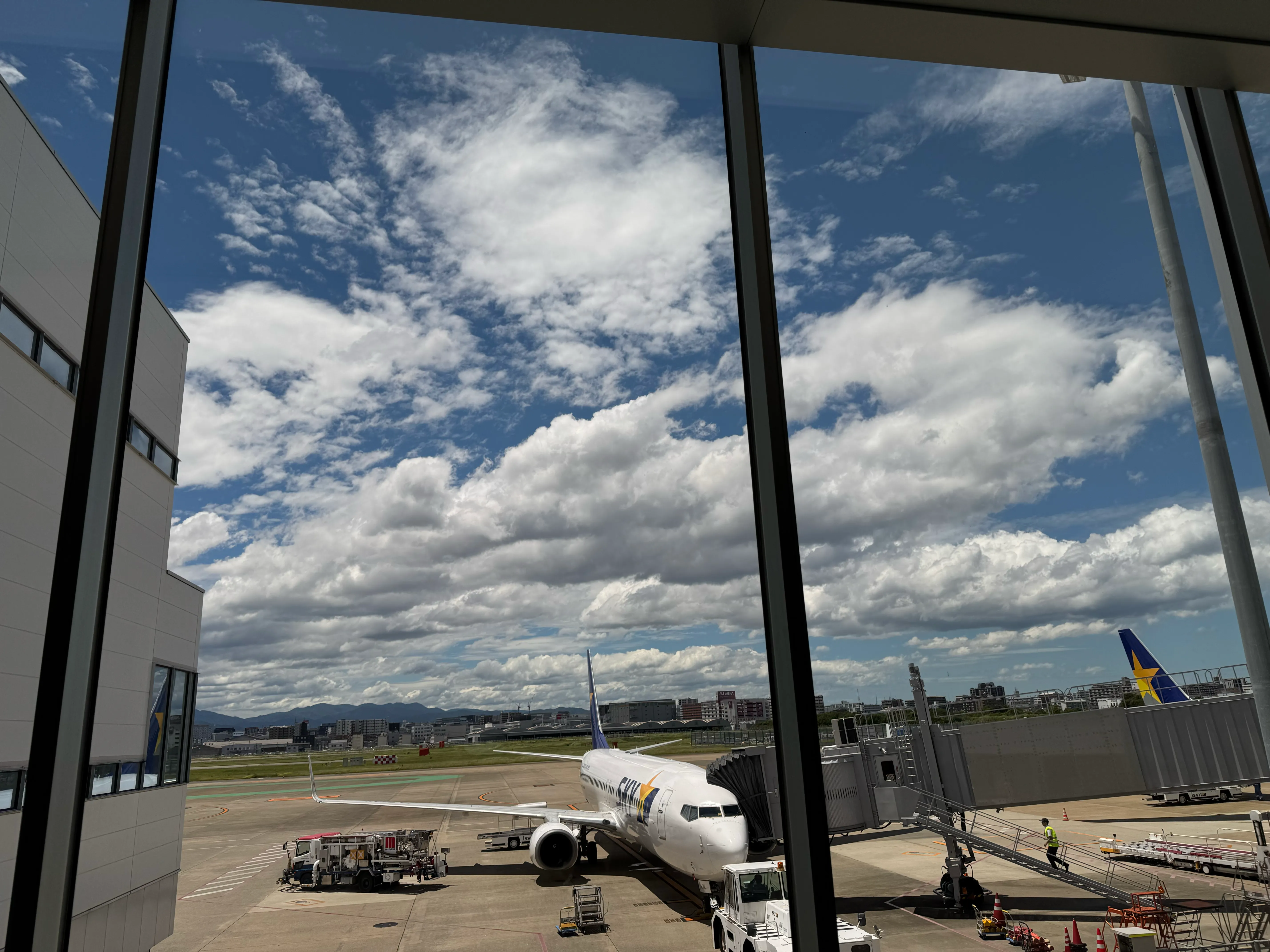 福岡空港のターミナルガラス越しに見えるスカイマークの航空機と夏の積乱雲
