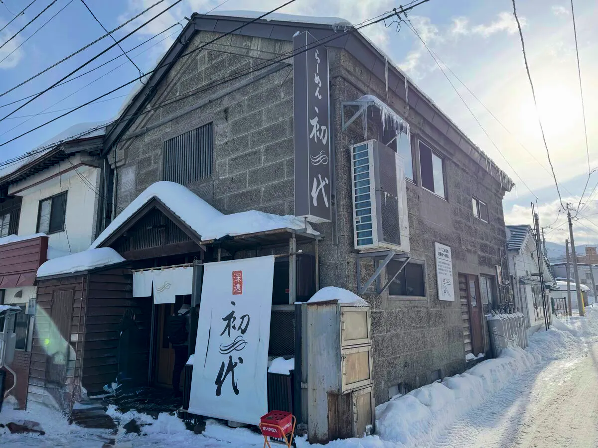 雪に覆われたらーめん初代の外観。「初代」の暖簾と看板が目を引く