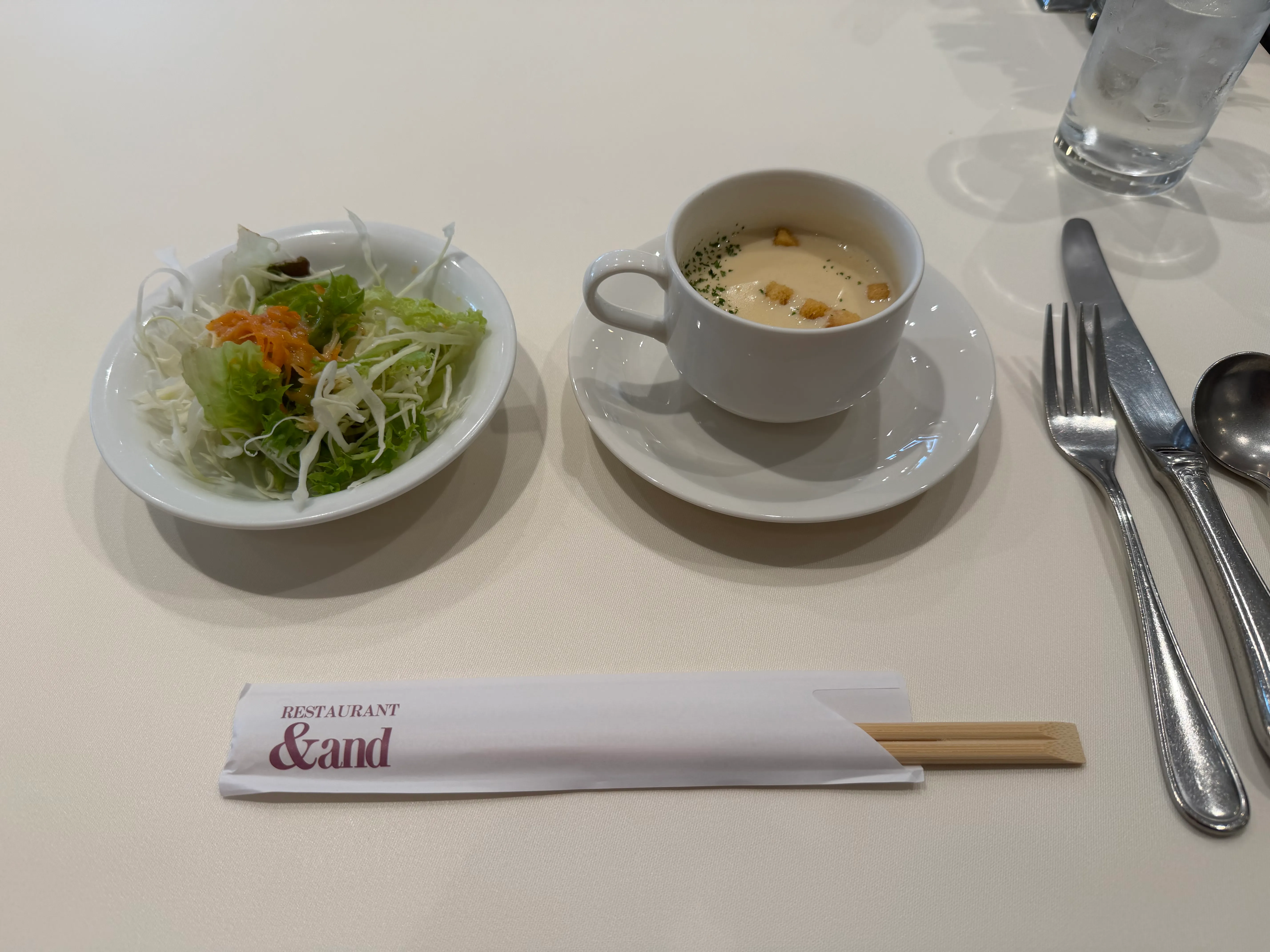 サラダとコーンスープの前菜セット。&#x26;andのお箸袋と並んで白いテーブルに置かれている