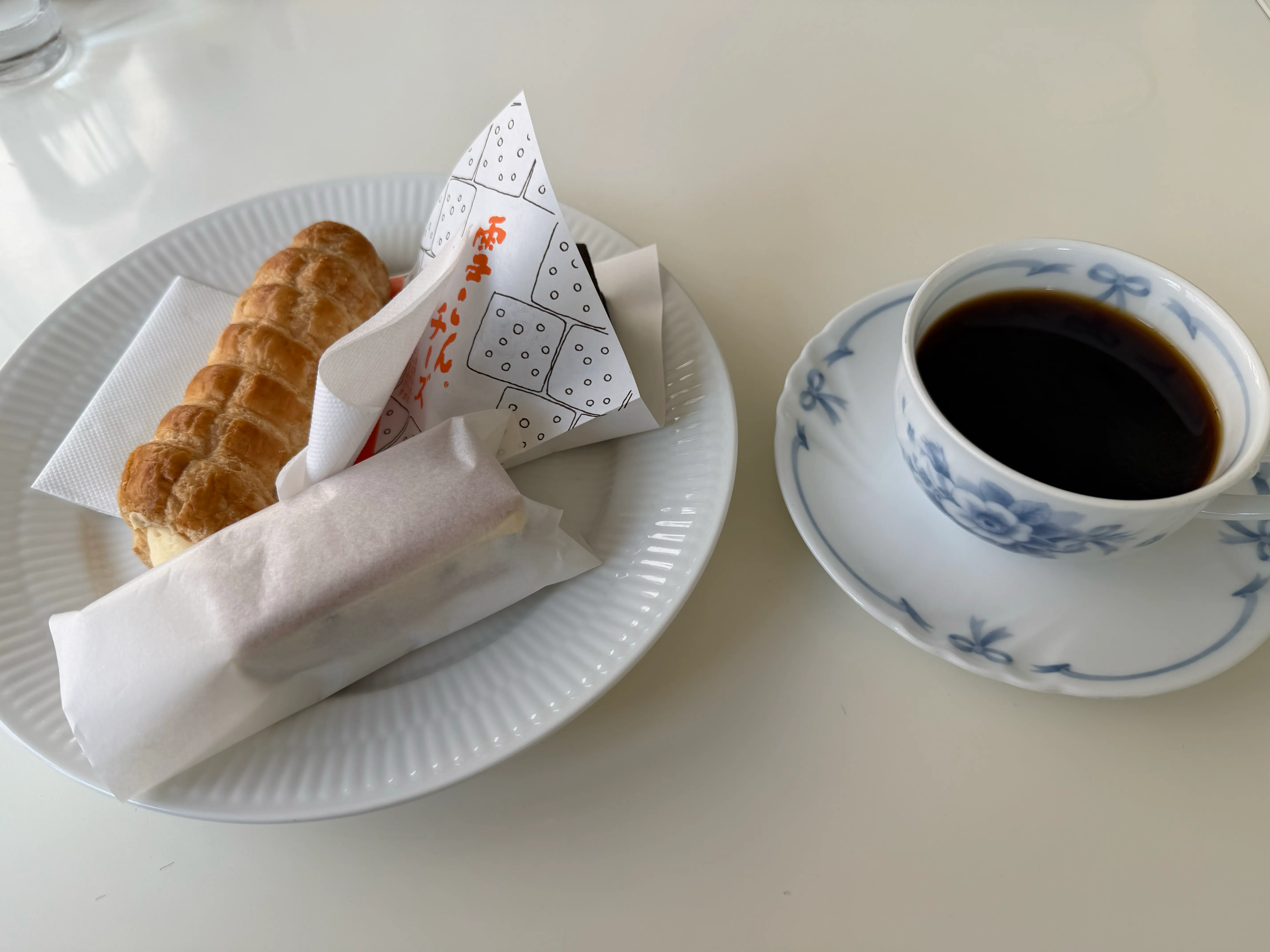 六花亭喫茶のセット。白い上品なプレートにバターサンドと雪やこんこが乗り、隣に六花模様のコーヒーカップが置かれている