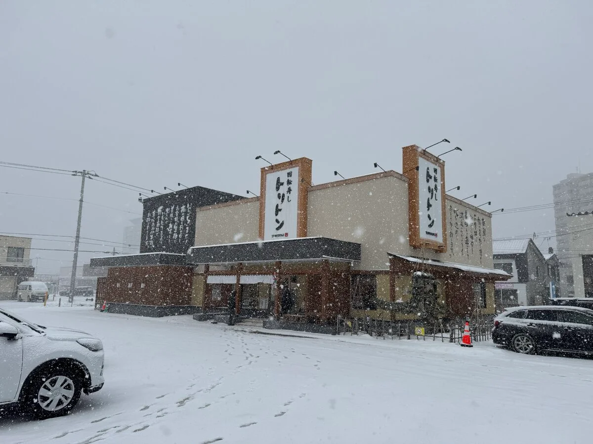 吹雪の中に立つ回転寿しトリトン 北8条光星店の外観